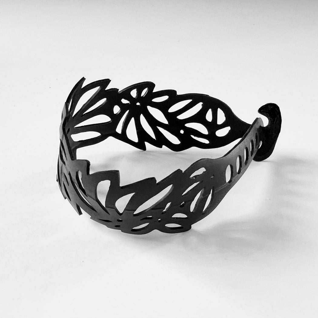 This bracelet was made by cutting intricate tropical flower and leaf designs into a bicycle inner tube. The bracelet is 1.25 inches wide. It has a t-shape clasp that fits into one of six holes making this bracelet adjustable and suitable for a wide range of wrist sizes.
