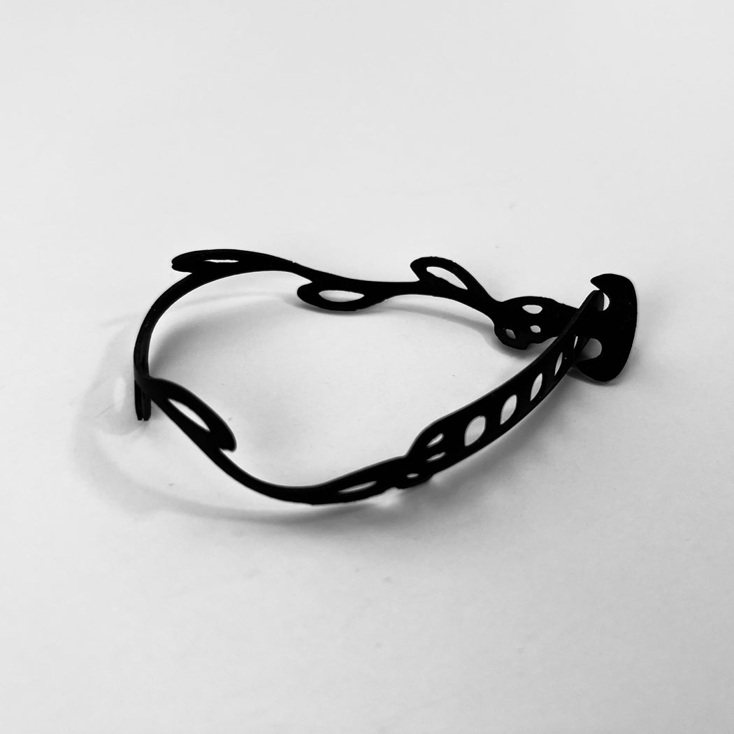 This bracelet was made by cutting intricate designs into a bicycle inner tube. This bracelet looks like a vine with tiny leaves spaced about an inch apart. It is about .25 inches wide. It has a t-shape clasp that fits into one of six holes making this bracelet suitable for a wide range of wrist sizes.