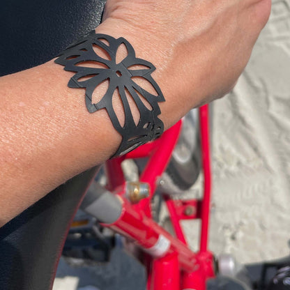 This bracelet was made by cutting intricate tropical flower and leaf designs into a bicycle inner tube. The bracelet is 1.25 inches wide. It has a t-shape clasp that fits into one of six holes making this bracelet adjustable and suitable for a wide range of wrist sizes.