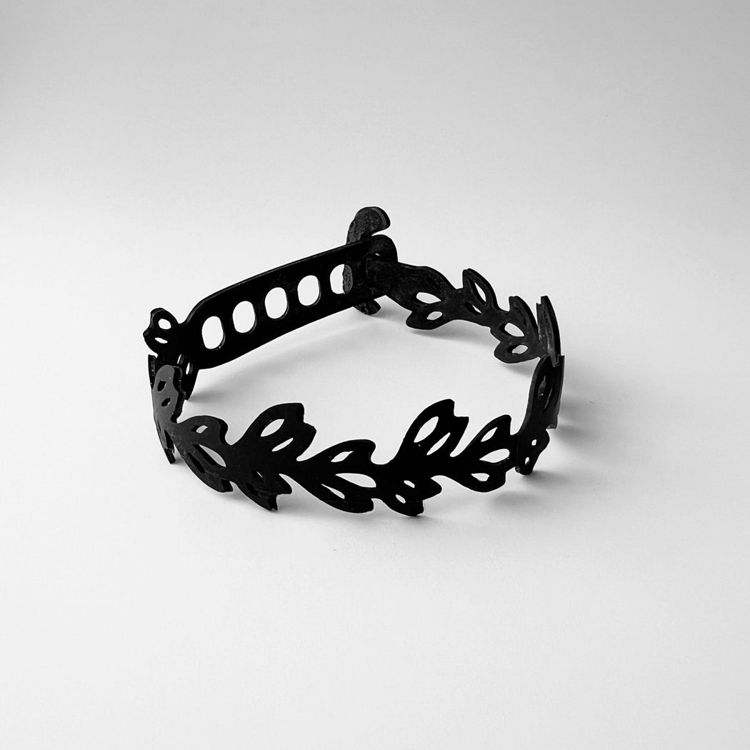 This bracelet was made by cutting tiny leaf patterns into a bicycle tube. The tiny leaves form a vine that is .75 inches at its widest point. It has a t-shape clasp that fits into one of six holes making it suitable for a wide range of wrist sizes.