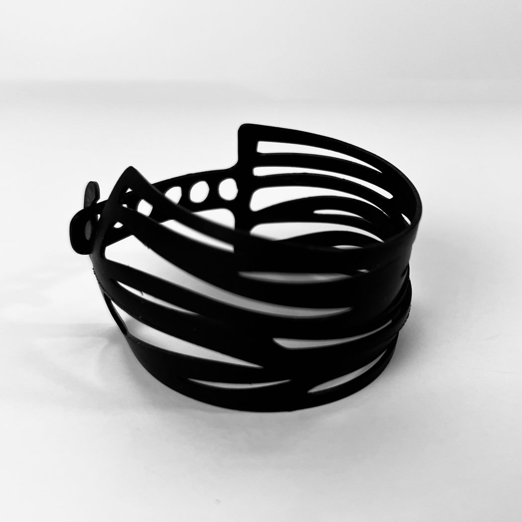 This bracelet was made by cutting intricate designs into a bicycle inner tube. It looks like a zebra pattern or a series of thin bracelets. It is 1.75 inches wide. It has a t-shape clasp that fits into one of six holes making this bracelet suitable for a wide range of wrist sizes.