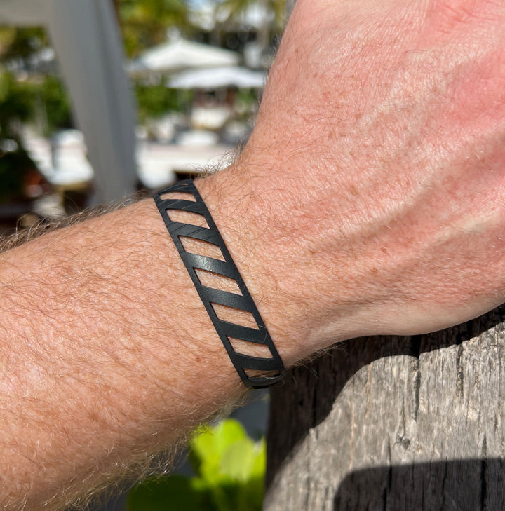 This bracelet was made by cutting the diver down or parallelogram shaped designs into a bicycle inner tube in a repeat pattern. The bracelet is .5 inches wide. It has a t-shape clasp that fits into one of six holes making this bracelet suitable for a wide range of wrist sizes.