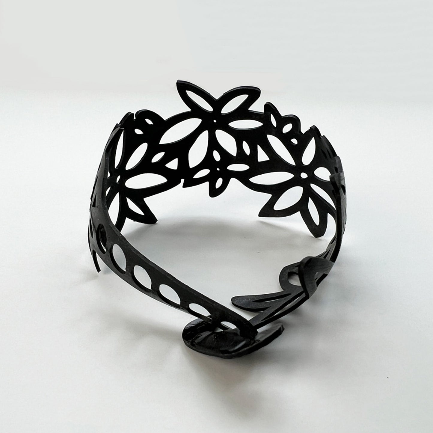 This bracelet was made by cutting intricate daisy designs into a bicycle inner tube. The bracelet is 1.25 inches wide. The biggest daisies are about an inch. It has a t-shape clasp that fits into one of six holes making this bracelet suitable for a wide range of wrist sizes
