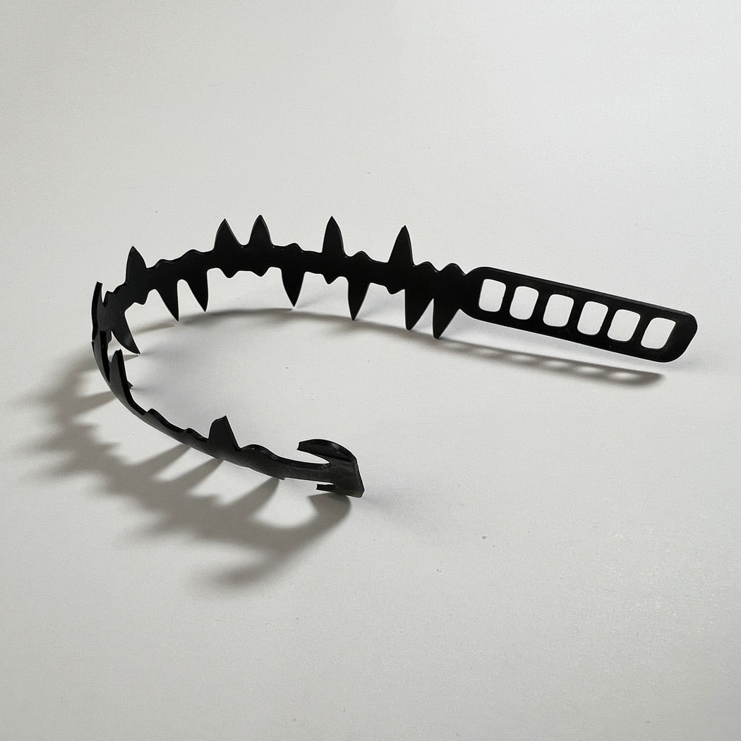 This bracelet was made by cutting intricate designs into a bicycle inner tube. It looks a series of spikes or shark teeth connected to a cord.  It is 1.25 inches wide. It has a t-shape clasp that fits into one of six holes making this bracelet suitable for a wide range of wrist sizes.