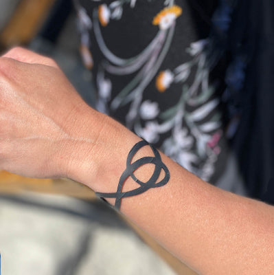This bracelet was made by cutting intricate designs into a bicycle inner tube. It looks like a ribbon layed out like a G Clef note. It is 1.25 inches wide. It has a t-shape clasp that fits into one of six holes making this bracelet suitable for a wide range of wrist sizes.