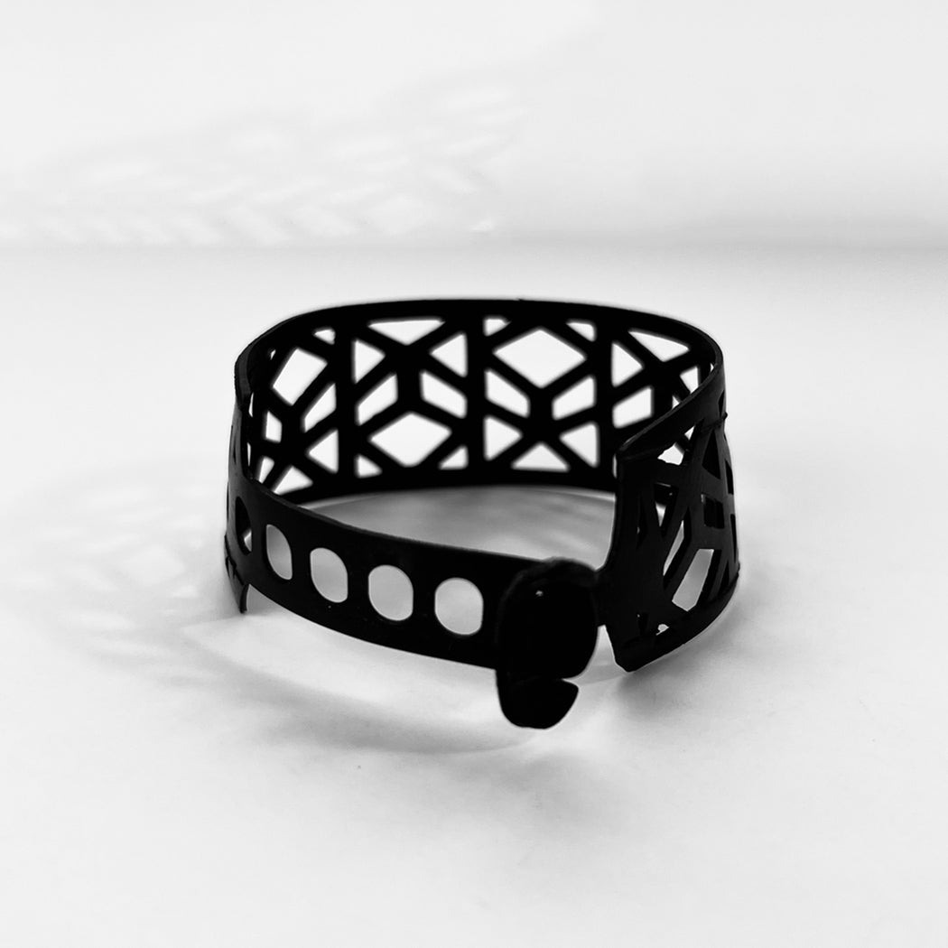 This bracelet was made by cutting intricate designs into a bicycle inner tube. looks like a criss cross vine in a repeat pattern. It has a tribal feel to it.  It is about 1.2 inches wide. It has a t-shape clasp that fits into one of six holes making this bracelet suitable for a wide range of wrist sizes.