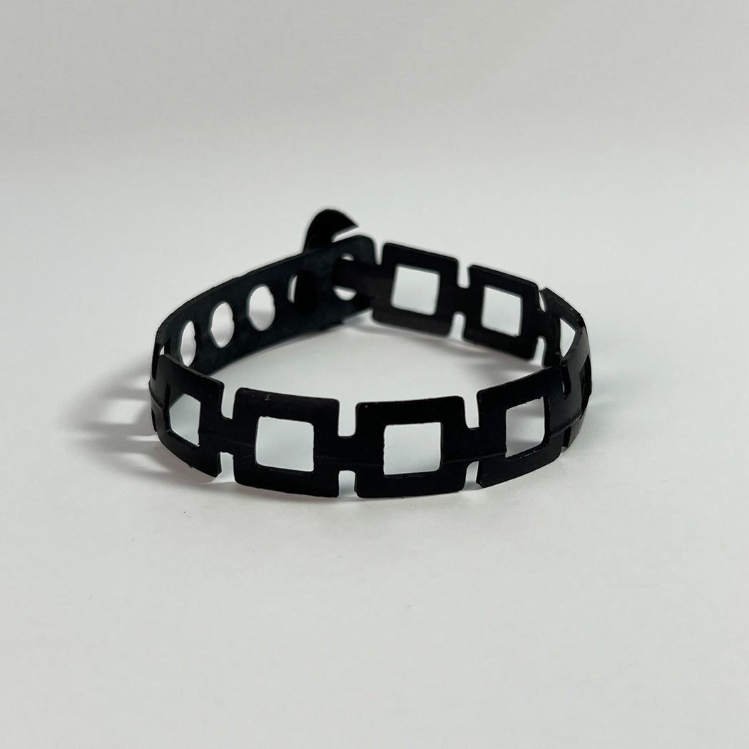 This bracelet was made by cutting intricate designs into a bicycle inner tube. This bracelet has a series of rectangle shapes linked together to form a chain. It is about .5 inches wide. It has a t-shape clasp that fits into one of six holes making this bracelet suitable for a wide range of wrist sizes.