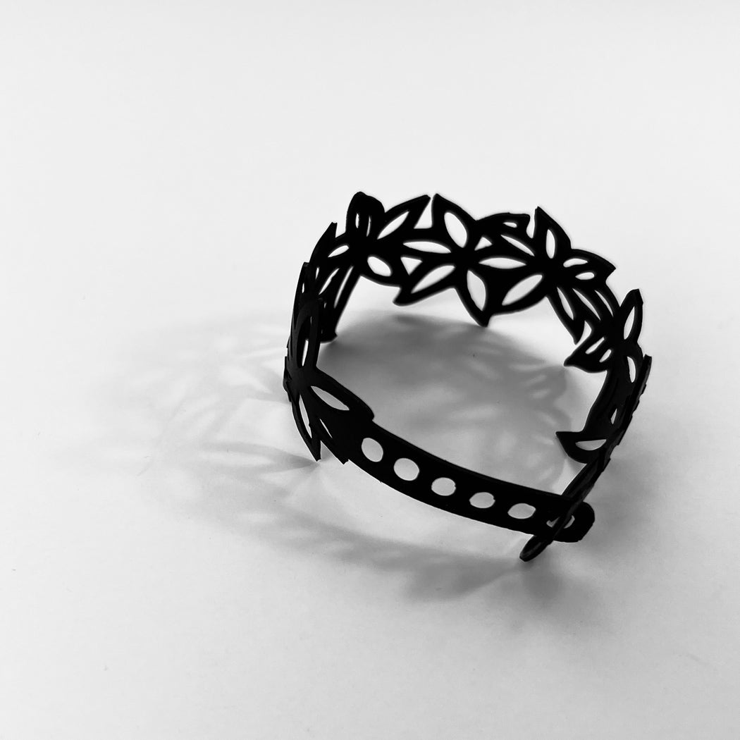 This bracelet was made by cutting intricate designs into a bicycle inner tube. This bracelet features a series of flowers with five petals making it 1.25 inches wide. It has a t-shape clasp that fits into one of six holes making this bracelet adjustable and suitable for a wide range of wrist sizes.