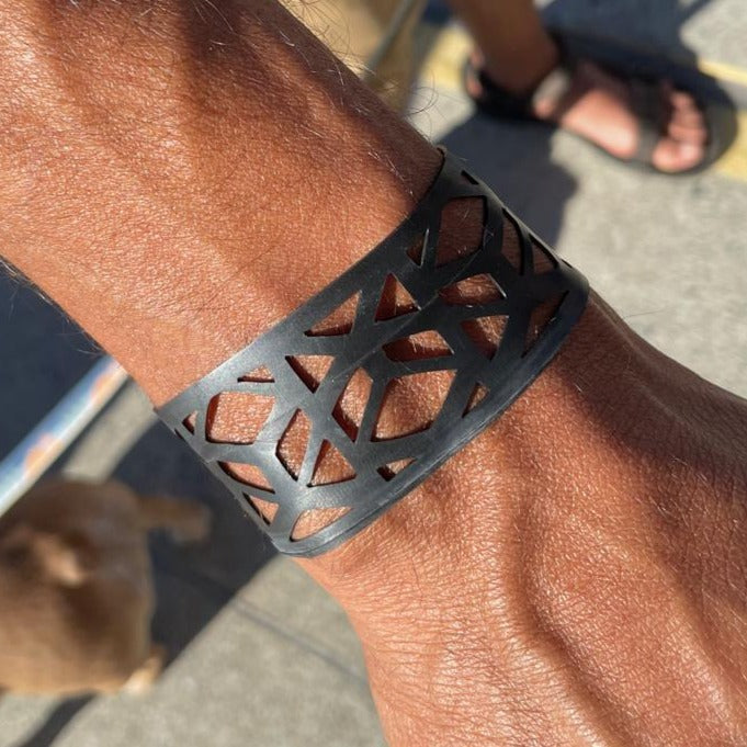 This bracelet was made by cutting intricate designs into a bicycle inner tube. It looks like a criss cross vine in a repeat pattern. It has a tribal feel to it.  It is about 1.2 inches wide. It has a t-shape clasp that fits into one of six holes making this bracelet suitable for a wide range of wrist sizes.